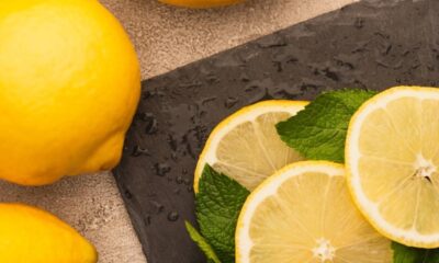 Dois limões inteiros, fatias de limão e folhas de hortelã sobre uma superfície escura molhada.