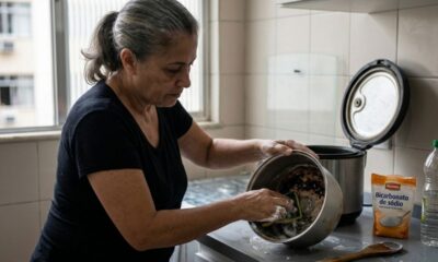 Mulher limpa panela queimada com esponja, usando bicarbonato de sódio e vinagre na cozinha.