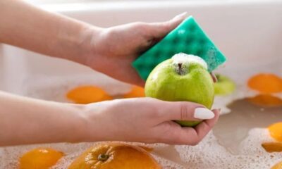 Mãos usando uma esponja verde para lavar uma maçã verde com espuma em uma pia.