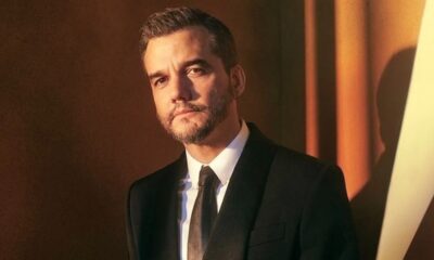 Ator Wagner Moura com barba e terno escuro, olhando à frente com expressão séria.