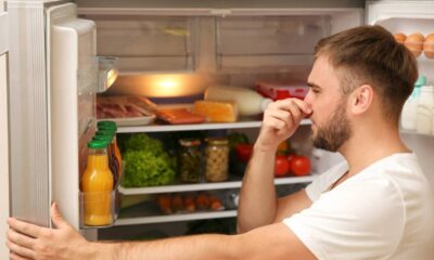 Homem com barba tampa o nariz ao abrir uma geladeira cheia de alimentos.