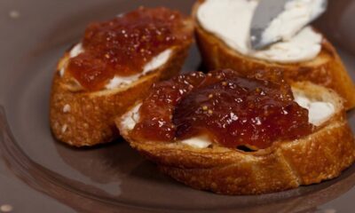 Três torradas com creme branco e geleia de figo caseira em prato marrom.