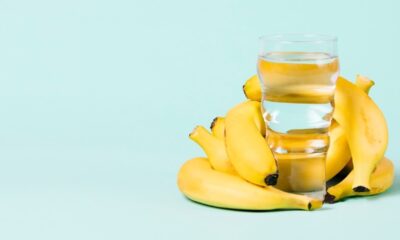 Copo de água transparente entre bananas amarelas maduras em um fundo azul claro.