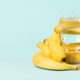 Copo de água transparente entre bananas amarelas maduras em um fundo azul claro.