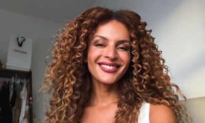 Gabriela Loran sorri para a câmera. Tem cabelos castanhos cacheados e batom vermelho escuro.