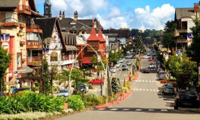 Rua com edifícios de arquitetura europeia, carros, decorações festivas e vegetação exuberante.