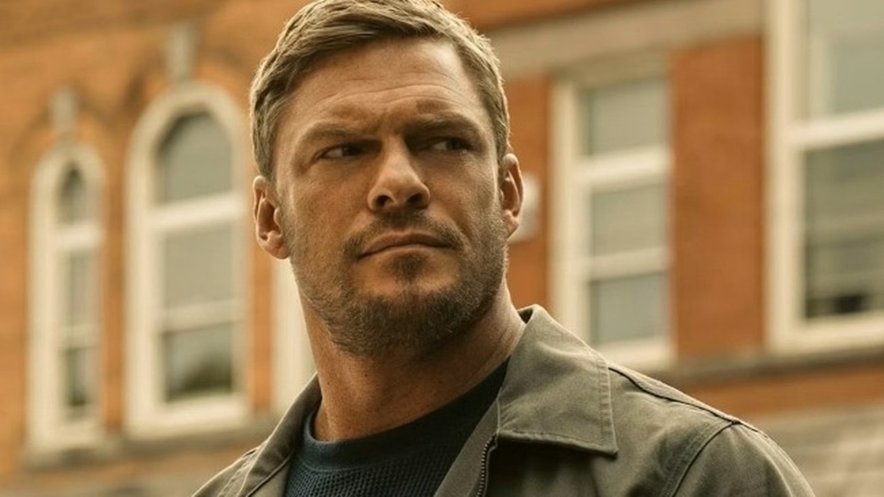 O ator Alan Ritchson, com expressão séria e barba por fazer, em imagem da série Reacher.
