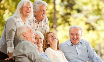 Seis idosos (três homens e três mulheres) sorrindo e rindo juntos, ao ar livre.
