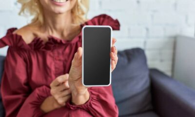 Pessoa sorridente segura smartphone branco com tela preta vazia, mostrando-o à câmera.