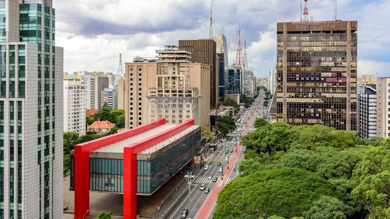 Vista aérea do MASP, Avenida Paulista, prédios e árvores em São Paulo sob céu nublado.