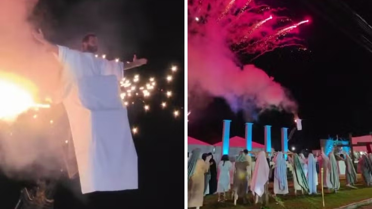 Ator em túnica branca com fogo no figurino e cena noturna de espetáculo com fogos de artifício.