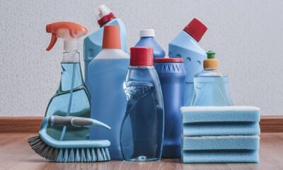 Garrafas azuis de produtos de limpeza, esponjas e escova em um piso de madeira.