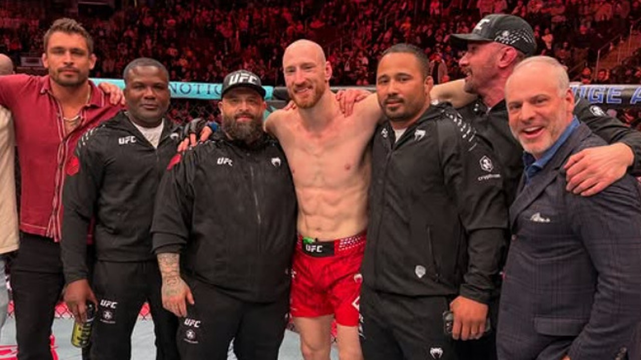 Joe Pyfer sem camisa celebra sorridente com sua equipe no octógono após a luta do UFC.