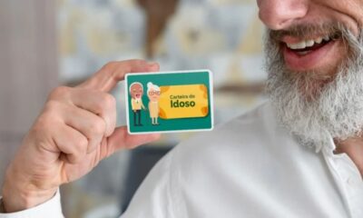 Homem sorrindo segurando a Carteira do Idoso, cartão verde com ilustrações de idosos.