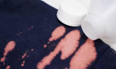 Tecido azul-marinho com manchas de descoloração e frasco branco de alvejante ao lado.