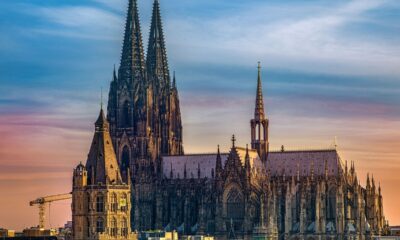 Catedral de Colônia e edifícios históricos sob céu degradê azul e laranja.