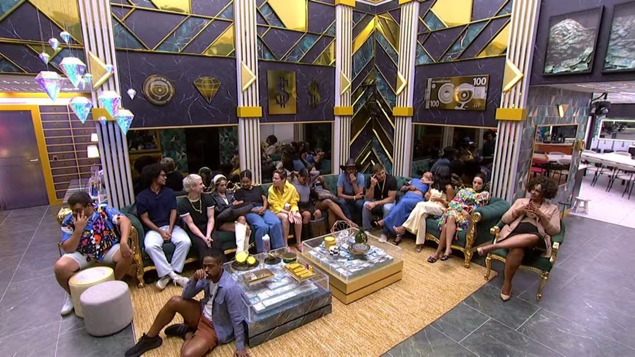 Grupo de confinados em sala de estar luxuosa com tema dinheiro, sentados em sofás e chão.