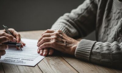 Mãos escrevendo documento enquanto mãos envelhecidas repousam sobre uma mesa de madeira.