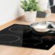 Cooktop de indução preto embutido em bancada de madeira com panela de metal brilhante.