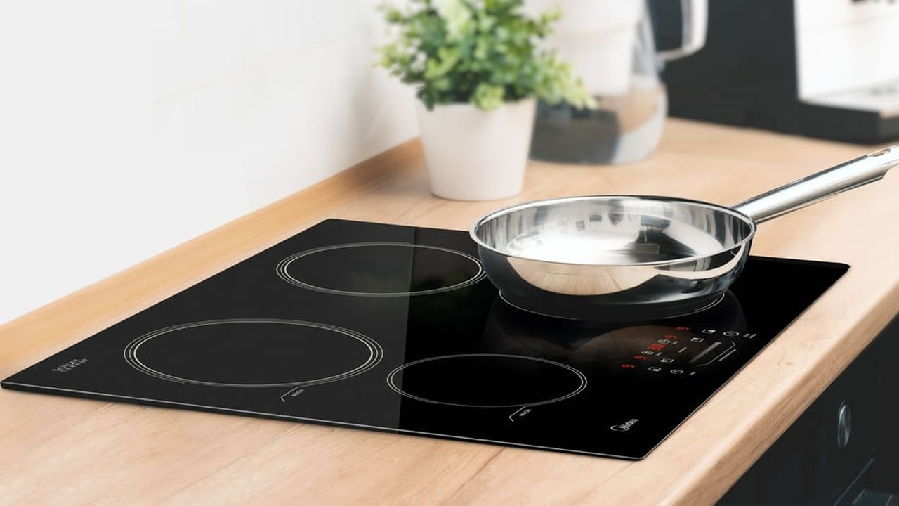 Cooktop de indução preto embutido em bancada de madeira com panela de metal brilhante.