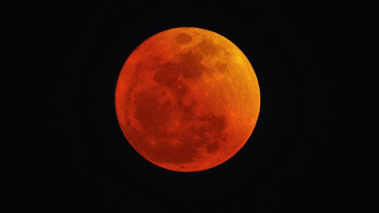 Uma lua cheia em eclipse total, exibindo uma coloração avermelhada contra um céu escuro.
