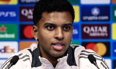 Jogador Rodrygo em coletiva, close-up, fundo com logos de patrocinadores.