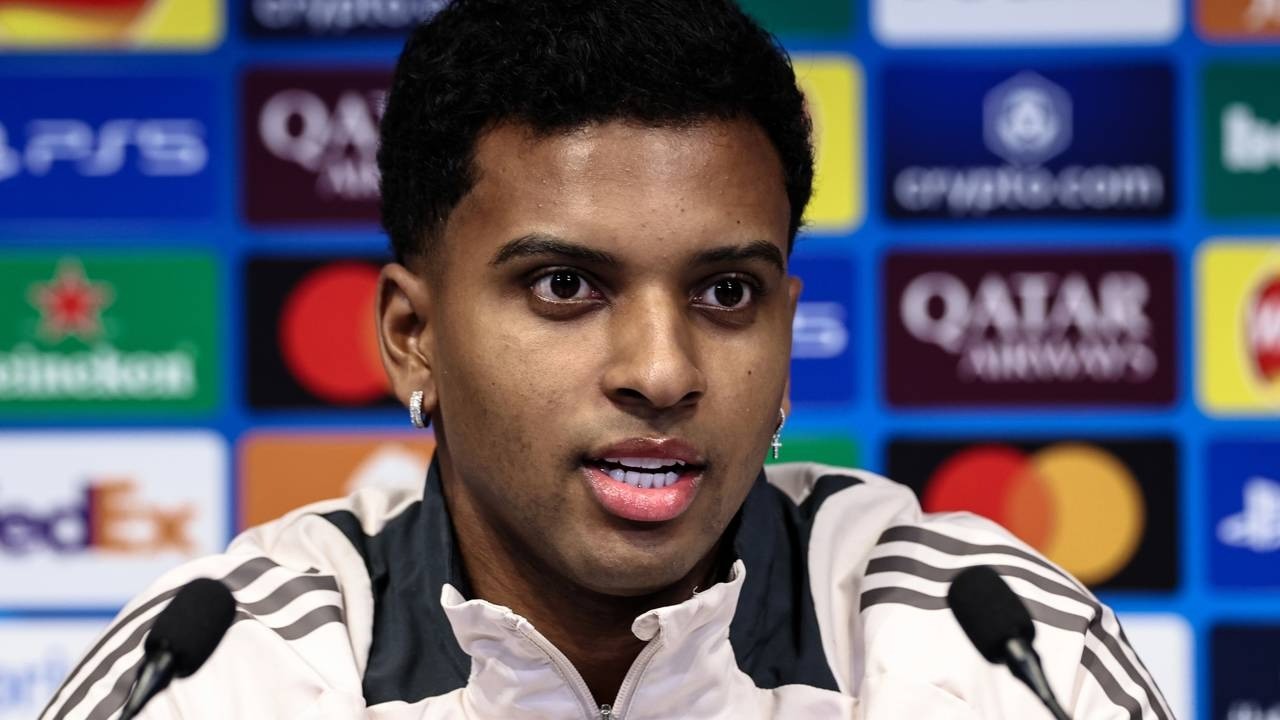 Jogador Rodrygo em coletiva, close-up, fundo com logos de patrocinadores.