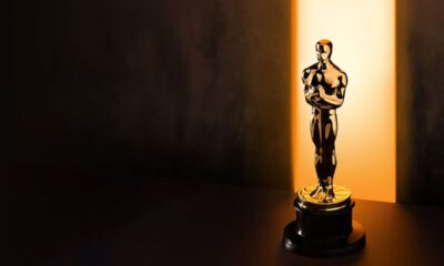 Estatueta dourada do Oscar sobre base escura, iluminada por uma forte luz vertical ao fundo.