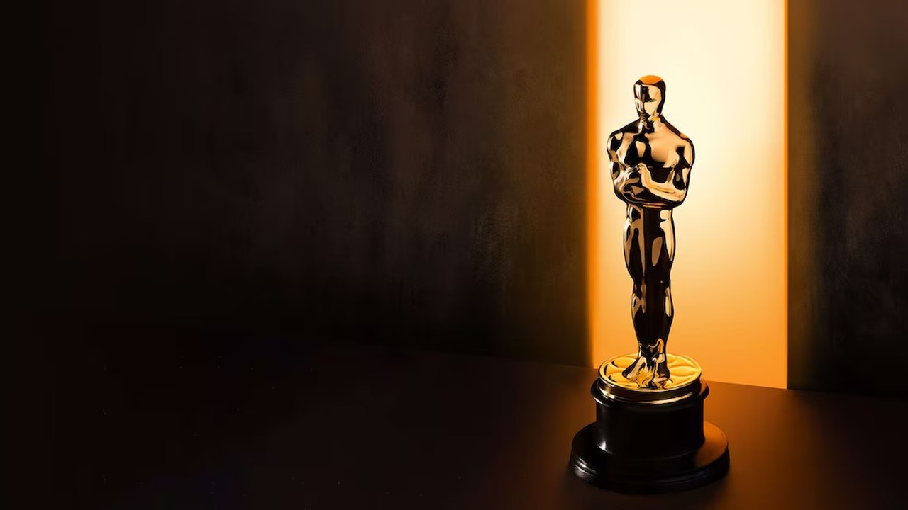 Estatueta dourada do Oscar sobre base escura, iluminada por uma forte luz vertical ao fundo.