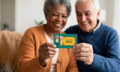 Casal de idosos sorrindo, segurando cartão verde 'Carteira do Idoso' com desenhos de idosos.