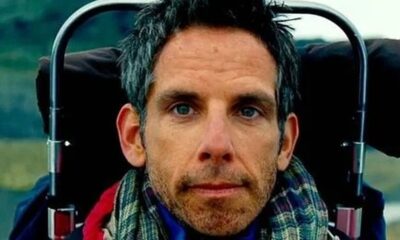 Rosto de Ben Stiller olhando para frente, cabelo grisalho, barba, olhos azuis, cachecol xadrez.