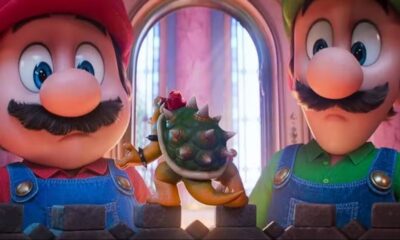 Mario e Luigi do filme, olhando à frente, com uma pequena figura de Bowser entre eles.