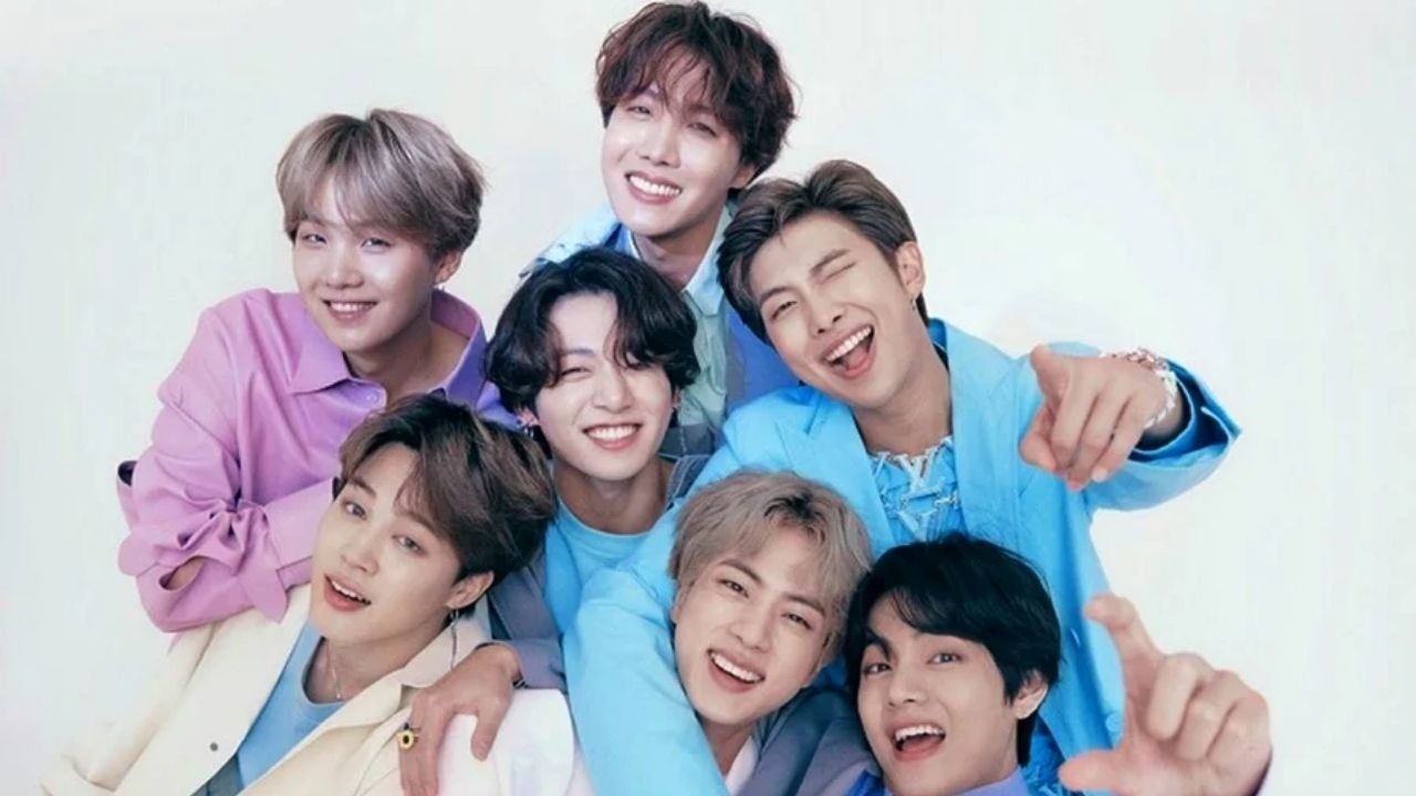 Sete membros do BTS sorriem, posando juntos em roupas coloridas vibrantes contra fundo branco.