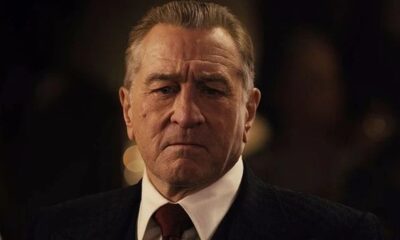 Close-up de Robert De Niro, homem mais velho, rosto sério, terno escuro, camisa branca.