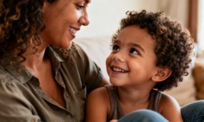 Mãe e filho sorrindo, um para o outro, em close-up, ambos com cabelo encaracolado.