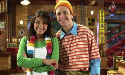 Sérgio Hondjakoff e Danielle Suzuki sorrindo, ele de gorro laranja, camisa listrada, ela de blusa verde, cachecol colorido.