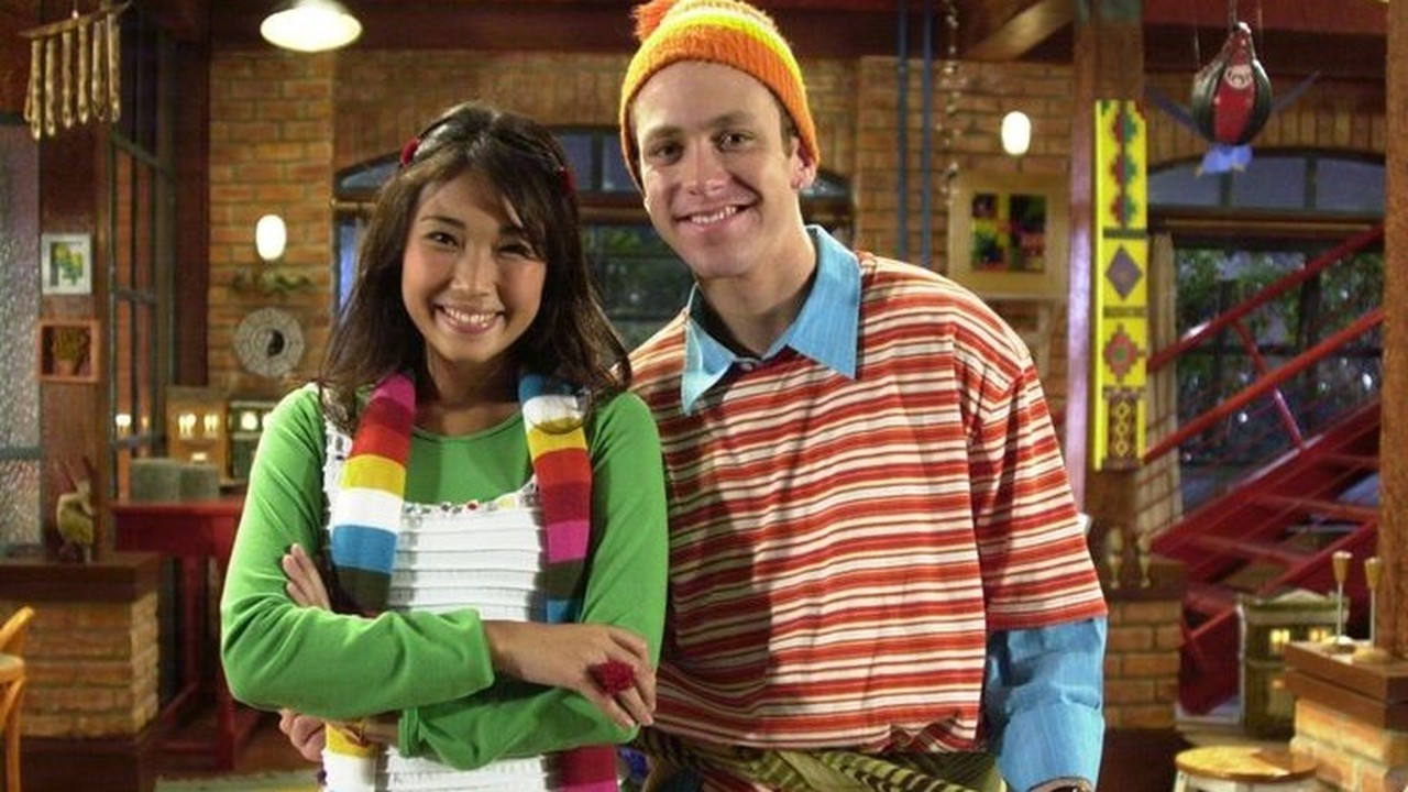 Sérgio Hondjakoff e Danielle Suzuki sorrindo, ele de gorro laranja, camisa listrada, ela de blusa verde, cachecol colorido.