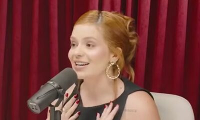 Viih Tube sorrindo em podcast com microfone, cabelo ruivo, brincos dourados e unhas vermelhas.