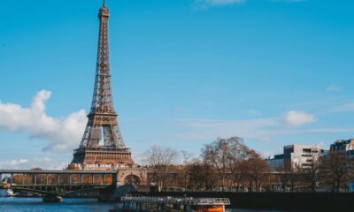 Torre Eiffel, Paris, com o rio Sena, uma ponte, barcos e céu azul.