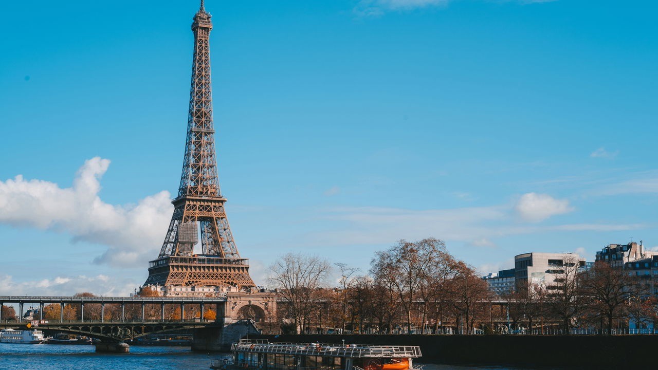 Torre Eiffel, Paris, com o rio Sena, uma ponte, barcos e céu azul.