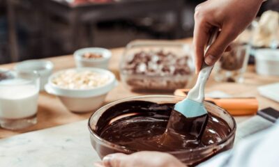 Pessoa mexendo chocolate derretido em tigela de vidro com espátula em ambiente de cozinha.