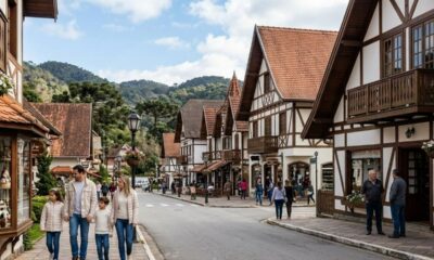 Rua em Campos do Jordão com prédios estilo enxaimel, pessoas caminhando e montanhas ao fundo.