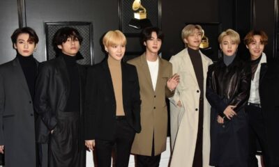 Sete homens do BTS posam em ternos e casacos contra fundo escuro com prêmios Grammy.