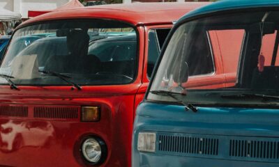 Frente de duas vans retrô, uma vermelha e uma azul, estacionadas, com faróis visíveis.