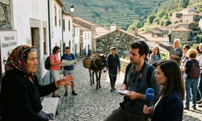 Mulher idosa com lenço na cabeça fala com repórteres em vila de paralelepípedos com burro.