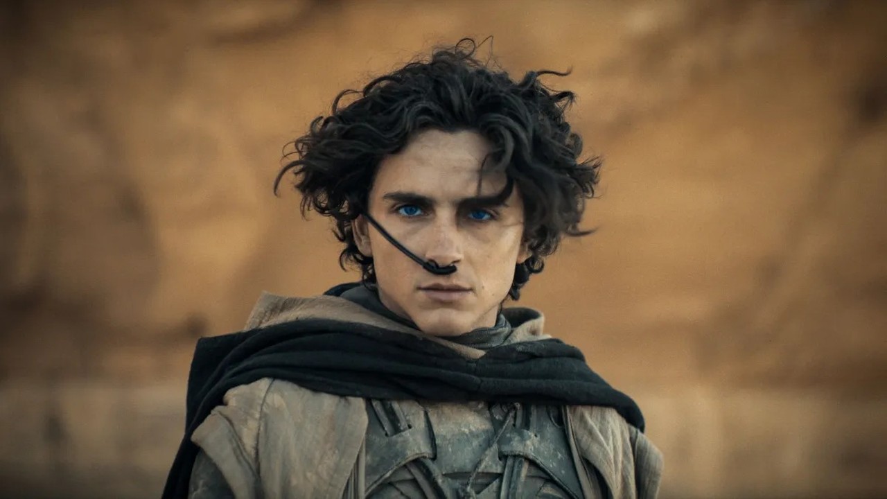 Close-up de Timothée Chalamet como Paul Atreides em Duna, com olhos azuis e traje desértico.