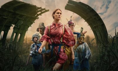 Grupo de sobreviventes em cenário pós-apocalíptico com estruturas destruídas e vegetação alta.