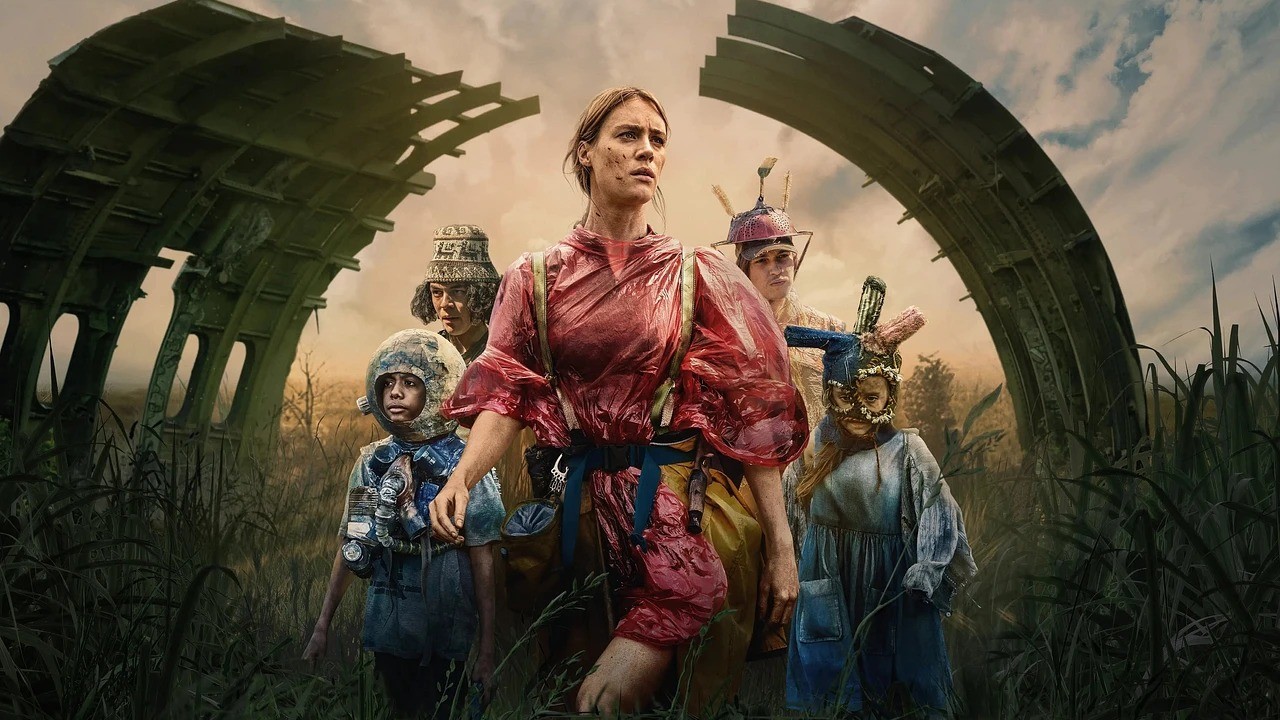 Grupo de sobreviventes em cenário pós-apocalíptico com estruturas destruídas e vegetação alta.