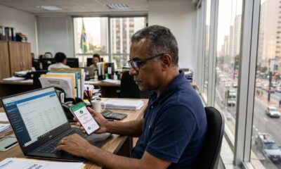 Homem em escritório com laptop e celular exibindo confirmação Pix, com cidade ao fundo.