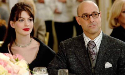 Stanley Tucci de óculos e Anne Hathaway de batom vermelho sentados em uma mesa.